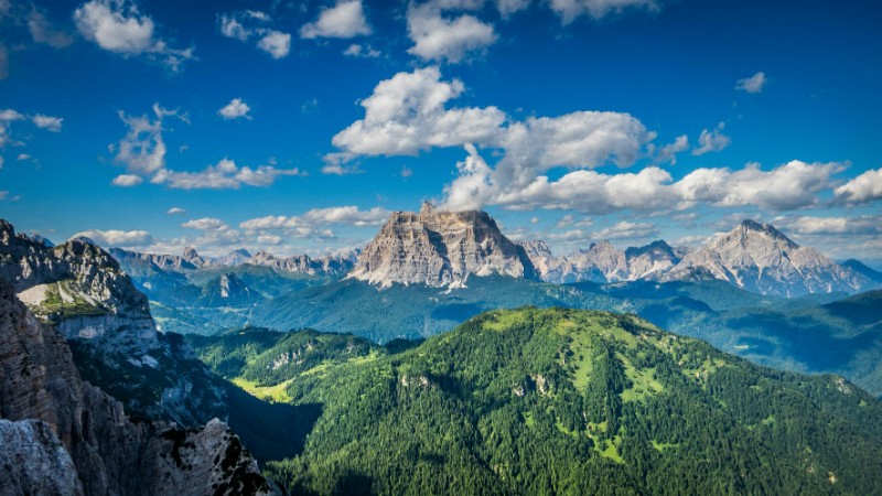Stunning aerial view of lush green forests and majestic rocky mountains under a bright blue sky., tags: il lusso - pexel